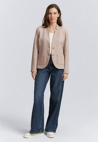 Blazer rose clair avec deux poches avant, coupe ajustée et fermeture à un bouton, associé à un jean denim bleu à jambes larges et des baskets blanches.