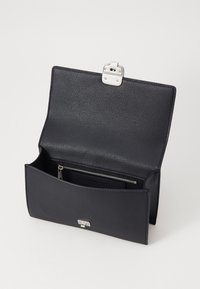 Geantă de mână din piele neagră cu suprafață texturată, clapetă din metal argintiu și un buzunar interior cu fermoar. Design deschis care oferă un spațiu de depozitare generos.