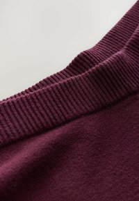 Bordo pulover s teksturiranim rebrastim izrezom, koji se odlikuje mekim pletenim materijalom i glatkim tijelom. Naglašava toplinu i udobnost.