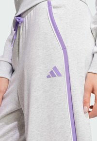 Jasnoszare dresy o miękkiej fakturze, z fioletowymi bocznymi paskami, elastycznym paskiem w talii i wytłoczonym lawendowym logo na udzie.