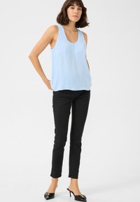 Haut sans manches bleu clair avec un col en scoop, associé à un jean skinny noir et des mules à talons noirs avec une boucle décorative.