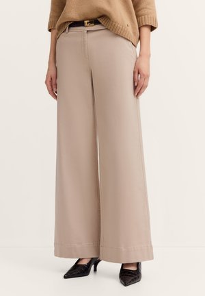 Beige weit geschnittene Hosen aus leichtem Stoff zeichnen sich durch eine glatte Textur und einen sauberen Abschluss aus und werden mit schwarzen spitzen Absätzen kombiniert.