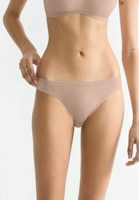 Beige nahtlose Slips aus weichem, elastischem Stoff. Sie haben einen niedrigen Schnitt, einen glatten Bund und eine minimale Bedeckung.