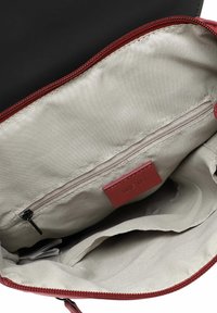 Intérieur d'un sac en tissu noir avec une doublure crème lisse, une fermeture éclair rouge et une poche zippée. Présente une petite étiquette de marque en rouge.