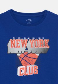 T-shirt in cotone blu con stampa grafica che presenta la scritta "NEW YORK", un pallone da basket e "CLUB" in bianco bold. Collo tondo e maniche corte.