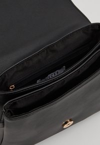 Černá kožená kabelka s otevřeným víkem, které odhaluje vnitřní látkovou podšívku a zipovou kapsu se zlatým táhlem.