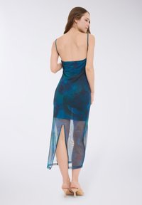 Sukienka bez rękawów w kolorze teal o gładkiej fakturze, z wysokim rozcięciem i przezroczystą dolną częścią. Prosty design i dopasowany krój, zestawiona z nude obcasami.
