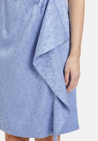 Hellblaues Kleid aus strukturiertem Stoff mit dezentem Muster, drapiertem Design und asymmetrischem Saum.