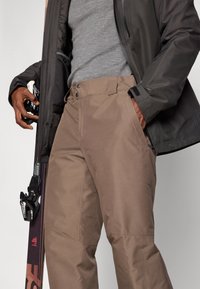 Ski pants in light brown fabric, featuring a straight cut, two front pockets, and a sleek, smooth texture with subtle stitching details.