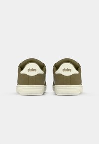 Par nogavic v olivno zeleni in bež barvi Etnies, prikazanih s hrbtne strani na enobarvni beli podlagi.
