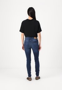 Top negro de manga corta, jeans ajustados azules con bolsillos traseros y zapatos tipo slip-on con estampado de leopardo. Tela suave, estilo ajustado, forma entallada.