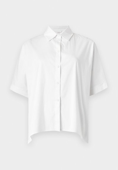 Chemise blanche à manches courtes avec boutons, col pointu et ourlet légèrement asymétrique, présentée sur fond clair uni.