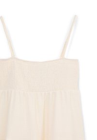 Light cream sleeveless top with smocked bodice and flowing skirt, made from soft, lightweight fabric; features thin adjustable straps.