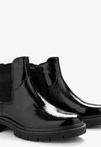 Stivaletti alla caviglia in pelle verniciata nera con pannelli laterali elasticizzati, finitura lucida e suola testurizzata. Dotati di zip per una facile calzata.