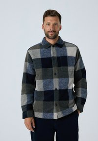 Multicolored flannel shirt featuring a large check pattern in dark blue, grey, and light grey, with a collar and front button closure.