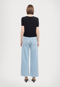 Top negro de manga corta combinado con jeans de pierna ancha de color azul claro. Los jeans cuentan con dos bolsillos traseros y un dobladillo sin terminar.