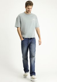 Camiseta gris claro de corte oversized, de manga corta y cuello redondo, combinada con vaqueros azules de tiro medio y zapatillas beiges con suelas blancas.
