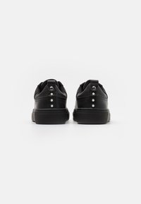 Czarne skórzane sneakersy z teksturowanymi akcentami, okrągłym kształtem noska i trzema dekoracyjnymi ćwiekami na zakładce pięty. Minimalistyczny design z solidną podeszwą.