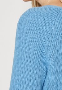 Maglione azzurro chiaro lavorato a maglia con texture a coste e scollo rotondo, che evidenzia il cucitura della spalla e il morbido dettaglio del tessuto.