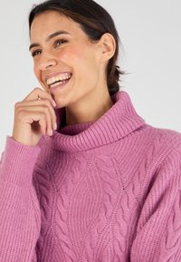 Maglione a maglia grossa in morbido rosa con colletto alto a coste. Presenta motivi testurizzati e maniche lunghe, evidenziando il suo design accogliente.