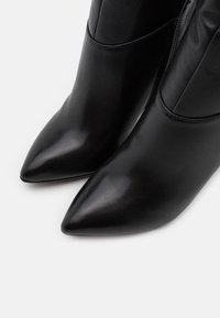 Botas de cuero negras hasta el tobillo con un diseño de punta afilada, textura suave y una silueta esbelta que cuenta con una cremallera lateral.