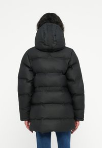 Crna podstavljena jakna s kapuljačom, koja sadrži kviltani dizajn i elastične manžete. Jakna ima glatku teksturu i širok kroj.