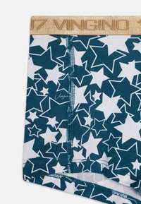 Teal bomuldsunderbukser med hvidt stjernemønster, med en guld elastisk taljebånd mærket "VINGINO." Bemærkelsesværdig syning.