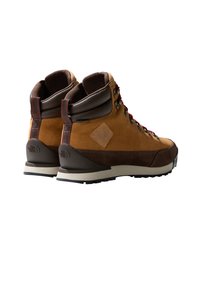 Botas de senderismo marrones con parte superior de ante y cuero, cordones rojos, un cuello acolchado y una suela de goma negra resistente para tracción.