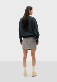 Felpa oversize grigio scuro con polsini a costine, abbinata a una mini gonna in corduroy grigio chiaro con due tasche posteriori. Calzini color crema e sneakers.