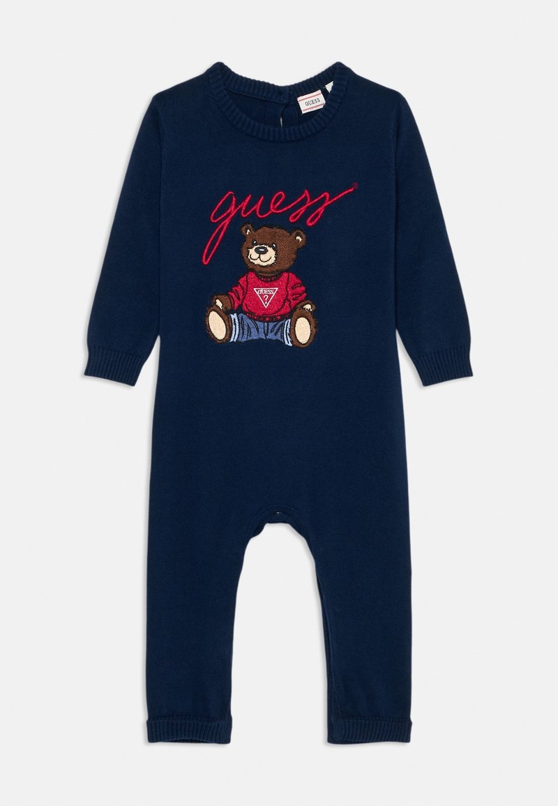 Grenouillère bébé à manches longues bleu marine avec un ours en peluche portant un sweat rouge Guess et le mot « guess » en écriture rouge au-dessus.