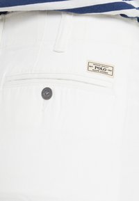 Vita bomullbyxor med en framficka med knappstängning och en beige etikett som läser "Polo Ralph Lauren" med etableringsdatum.