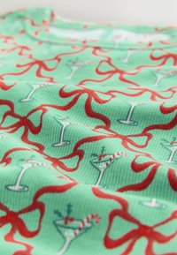 Green ribbed fabric with a repeating pattern of red ribbons and cocktails, featuring cherries and striped straws, emphasizing texture and color.