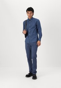 Kék ing, apró logóval, kék nadrággal és fekete cipővel összeillő kombinációval. Slim fit és sima textúrájú.