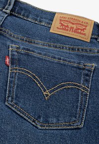 Τζιν τζιν με μια μόνο πίσω τσέπη με ορατή χρυσή ραφή και κόκκινη ετικέτα. Η μέση έχει μια καφέ δερμάτινη ετικέτα με στοιχεία επωνυμίας.