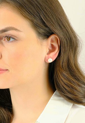 Perlenstecker mit einer glatten, runden Oberfläche; in einer einfachen Metallfassung eingesetzt; am Ohr eines Modells getragen, kombiniert mit einer weißen Bluse.