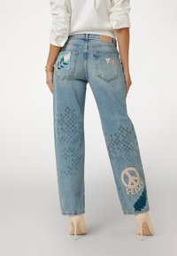 Šviesiai mėlyni, aukštu liemeniu džinsai su tiesiomis kojomis, puošti siuvinėjimais su lapais ir taikos ženklu ant nugaros, taip pat su subtiliais langeliais.