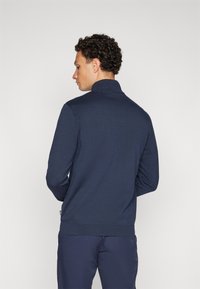 Pullover tricotado azul-marinho com colarinho alto e punhos canelados. Apresenta uma superfície texturizada subtil e um design ajustado.
