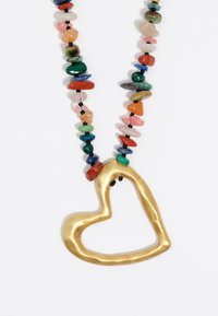 Colgante en forma de corazón de oro sobre un collar de cuentas que presenta piedras multicolores y separadores negros, creando una textura y diseño en capas.