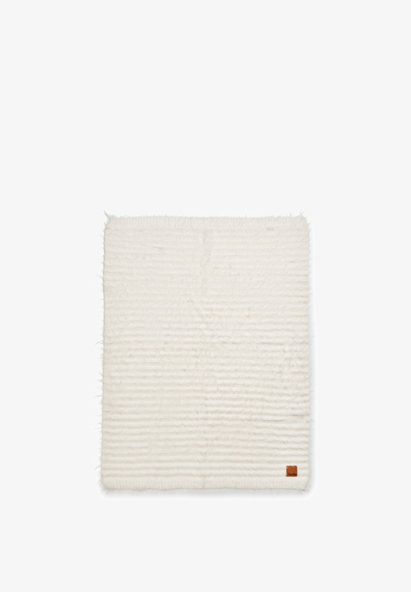 Suuri, kuviollinen vaaleankermanvärinen matto, jossa on pehmeä, tekstuurinen pinta. Matossa on hillittyjä raidallisia kuvioita, ja yhdessä kulmassa on pieni nahkainen brändiläpyskä.