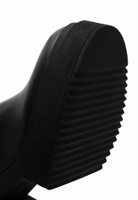 Black shoe sole featuring a textured rubber material with horizontal ridges and a rounded edge for added grip.
