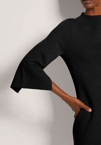 Schwarzes geripptes Kleid mit dreiviertellangen Glockenärmeln. Geschmeidige Textur, figurbetonte Form und dezente Seitentaschen. Einfaches, elegantes Design.