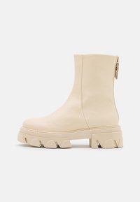 Cremefarbene Leder-Stiefelette mit einer robusten, strukturierten Gummisohle, seitlichem Reißverschluss für den Verschluss und einer glatten Textur.