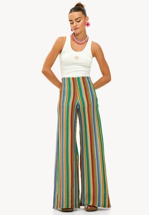 Pantalons évasés taille haute colorés avec un motif de rayures verticales en rouge, vert, violet et bleu. Associés à un débardeur blanc.