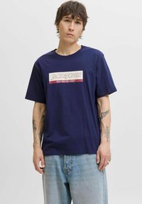 Marineblå bomulds t-shirt med en bokslogo, der har "JACK & JONES" og "SINCE NINETEEN NINETY" i hvid og maroon, afslappet pasform, kortærmet.