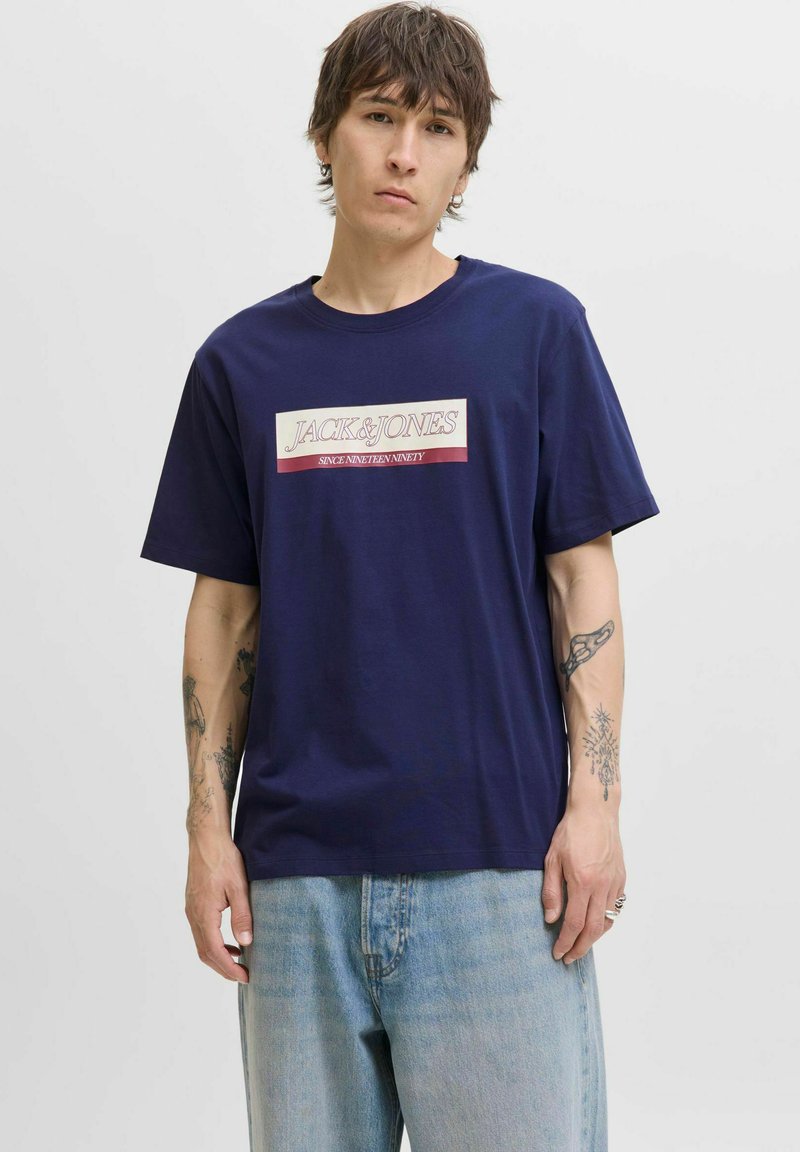 Marineblå bomulds t-shirt med en bokslogo, der har "JACK & JONES" og "SINCE NINETEEN NINETY" i hvid og maroon, afslappet pasform, kortærmet.