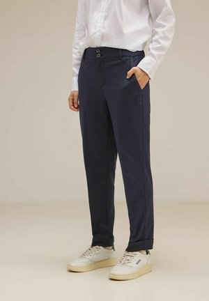 Pantaloni navy realizzati in un tessuto con una sottile trama, dotati di chiusura a due bottoni, tasche laterali e risvolti. Indossati con sneakers bianche.