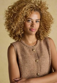 Brązowa bezrękawnik o gładkiej fakturze, okrągłym dekolcie i trzech złotych guzikach z przodu. Miękka, ciepła tkanina z subtelnymi wzorami.