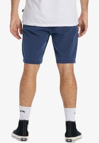 Navyblaue Baumwollshorts mit gerade geschnittenem Stil und umgeschlagenen Säumen, kombiniert mit schwarzen Sneakers im hohen Schnitt und weißen gerippten Socken.