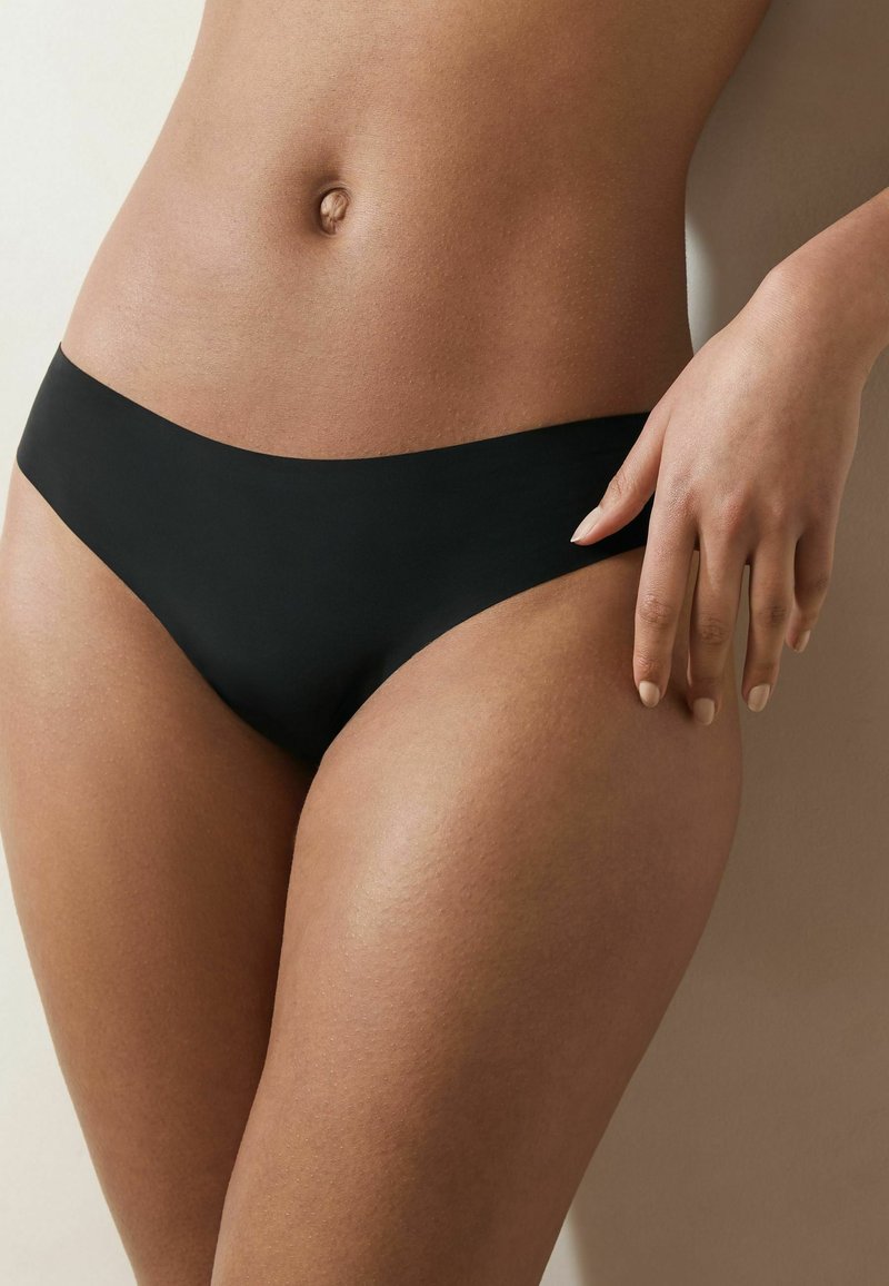 Black seamless bikini brief featuring a smooth texture and high-cut design, resting below the waist, with a hand positioned on the hip.