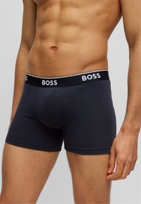 Tumesinine puuvillane bokseripüksid musta elastse vööga, millel on valge "BOSS" logo. Lähedalt sobiv disain sujuva tekstuuriga.